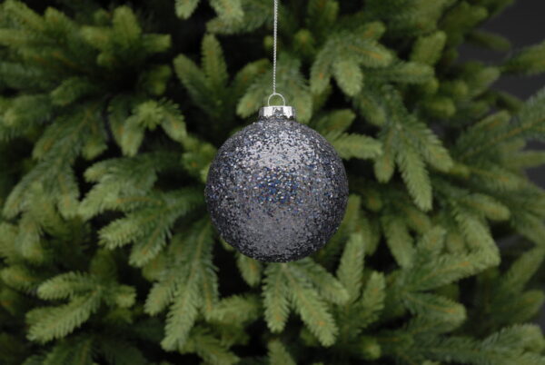 A silver Christmas bauble hanging from a pine tree.