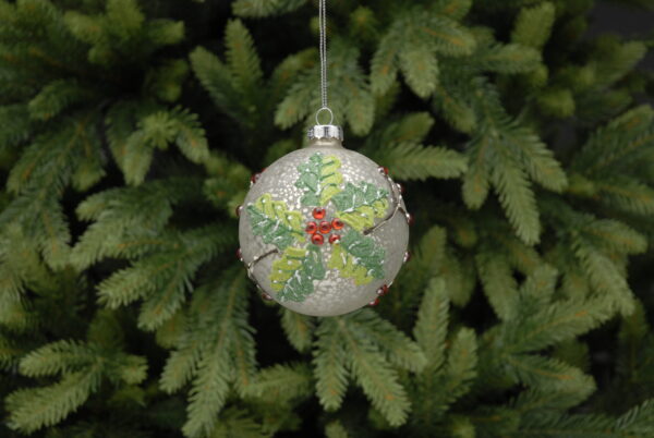 A Metallic, crackle glass bauble with holly design hanging from a pine tree.