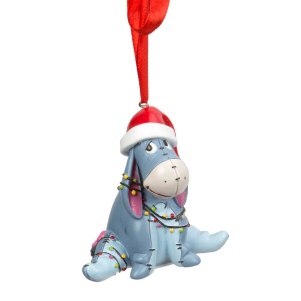 Eeyore, a lilac patchwork donkey toy, is suspended from a red ribbon, and is wearing a santa hat, wrapped up in fairy lights. Eeyore, from Disneys Winnie the Pooh is made of ceramic, and is designed to hang from the tree.