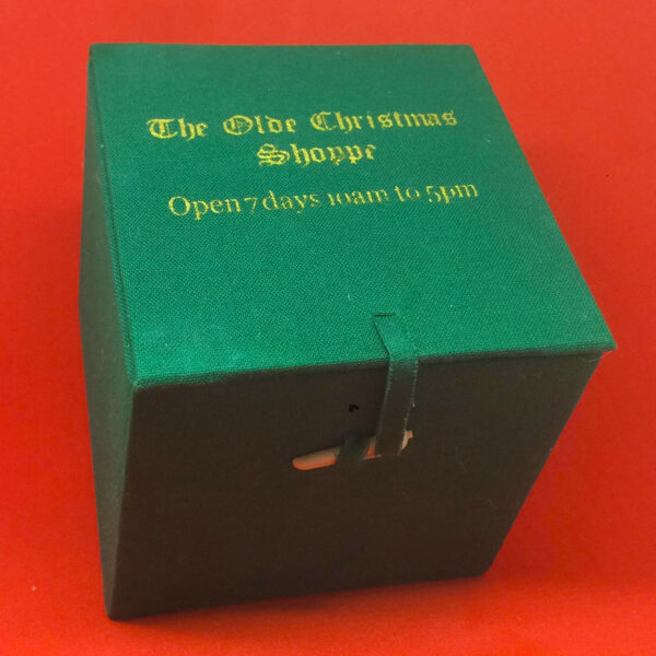 A green gift box with the words 'The olde Christmas Shoppe Open 7 Days 10am to 5pm