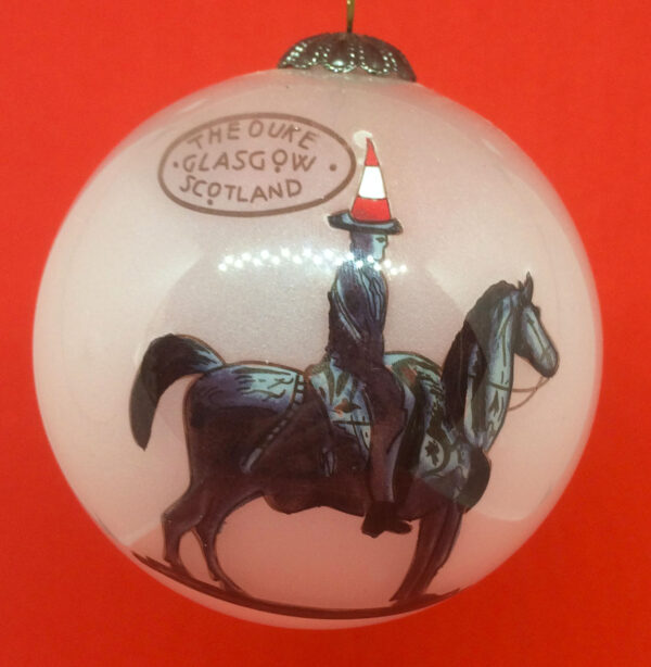 A beautiful handpainted bauble featuring the Iconic Duke of Wellington statue in Glasgow with his Traditional traffic cone on his head. This smokey white glass bauble shows the Duke of Wellington on his horse in shades of black and grey. On his head sits a traffic cone depicted in orange with a white band around the middle. Tope left of the duke is a logo that says 'THE DUKE, GLASGOW ,SCOTLAND' on three llines in an oval.