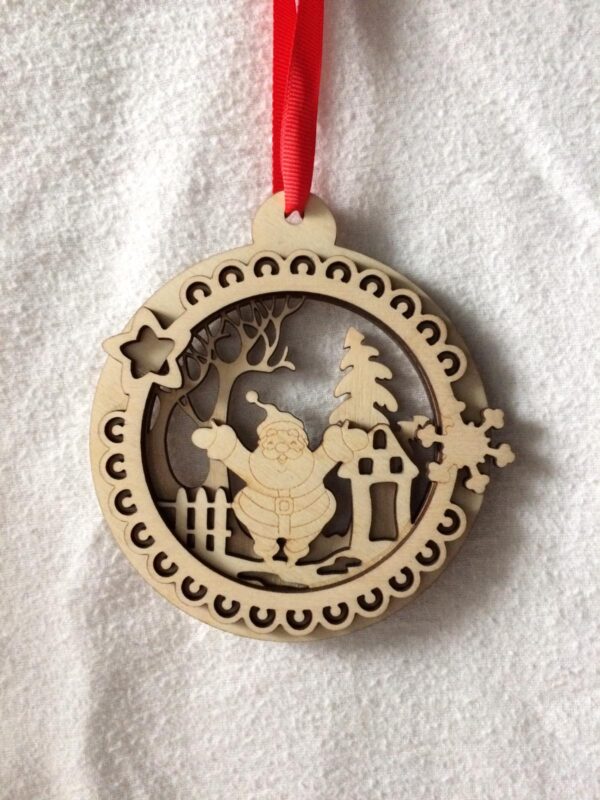 A round decorative 3D laser cut wooden tree hanging decoration with a cheerful Santa Claus in a festive scene in the middle hanging on a red ribbon.