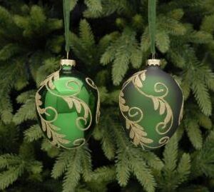 Two egg shaped green hanging baubles with gold glitter swirling vine and leaf decoration. The bauble on the left is a metallic green whilst the one on the right is a matt green. Both hang from a green voile ribbon and are shown against a background of green Christmas tree branches.