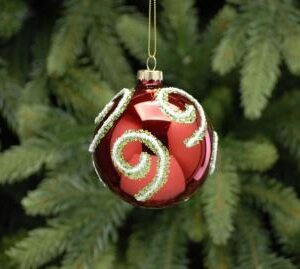 A red metallic looking glass Christmas bauble with green and white glitter swirls all over it hanging on a gold thread.