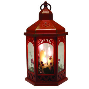 A hexagonal shaped red plastic lantern with gold accents and cut away deatils on the top and side panels. It is filled with three lit battery operated candles and festive foliage and red berries.