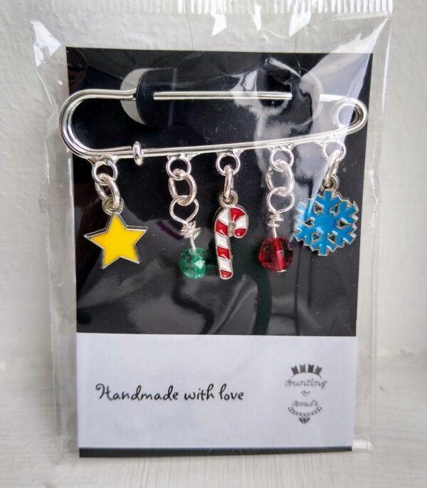 A Festive Brooch, made from a silver kiltpin with festive charms including a yellow star, a green faceted bead, a cute red and white candy cane, a red faceted bead and a blue snowflake. Hand made with love by Bunting & Beads.