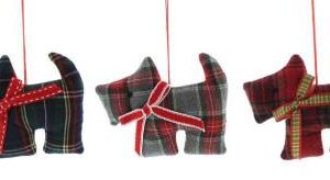 Three tartan fabric scottish terrier Christmas tree decorations. The dog on the left is made of dark green and blue tartan fabric and has a red bow with white stitching around his neck. The dog in the middle is made of grey and red tartan fabric and has a red bow with white trim around his neck. The dog on the right is made of red and black tartan fabric and has a green check bow with red trim around his neck.