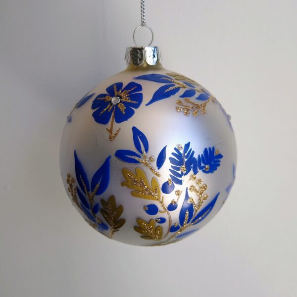 A matt white glass Christmas tree bauble decorated with colbalt blue and matt gold flowers and leaves with gold glitter detail and white diamante jewels.