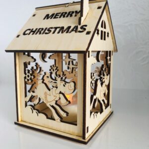 A 3D laser cut wooden tea light holder in the shape of a house. The words 'Merry Christmas' have been cut out of the roof and a cut out leaping reindeer design can be seen on the sides of the house. A battery operated tea light illuminates from with in.