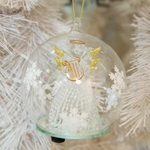 A pre-lit clear glass dome with white snowflakes around the outsides hangs from a gold thread. Inside the dome is a handmade glass angel wth a delicate lattice skirt and gold glitter tipped wings. She is holding a matt gold glass harp which matches her halo. On the bottom of the dome you can see the swith that operates the LED lights inside.