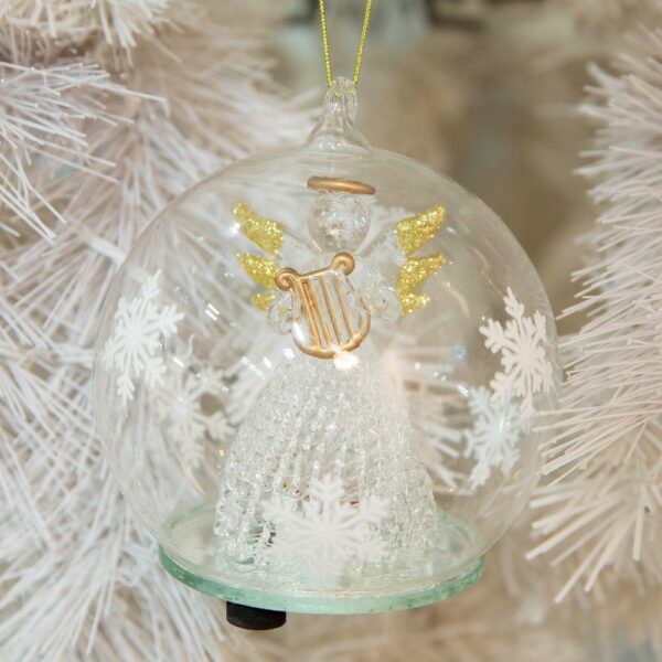 A pre-lit clear glass dome with white snowflakes around the outsides hangs from a gold thread. Inside the dome is a handmade glass angel wth a delicate lattice skirt and gold glitter tipped wings. She is holding a matt gold glass harp which matches her halo. On the bottom of the dome you can see the swith that operates the LED lights inside.