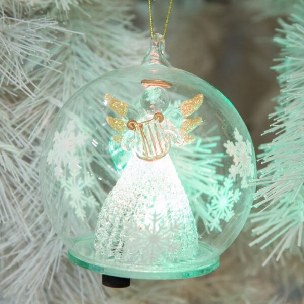 A pre-lit clear glass dome with white snowflakes around the outsides hangs from a gold thread. Inside the dome is a handmade glass angel wth a delicate lattice skirt and gold glitter tipped wings. She is holding a matt gold glass harp which matches her halo. On the bottom of the dome you can see the swith that operates the LED lights inside.