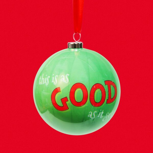 A decoupage christmas tree bauble from 'The Grinch' collection The bauble is green and has text on it that reads 'this is as GOOD as it gets' and hangs from a red ribbon. Shown against a red background.