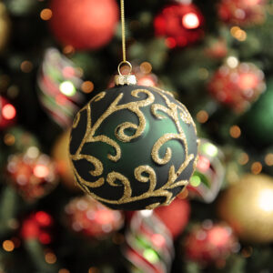 A matt dark green, moulded glass Christmas tree bauble decorated with swirling gold glitter vines all over. hanging from a gold string.