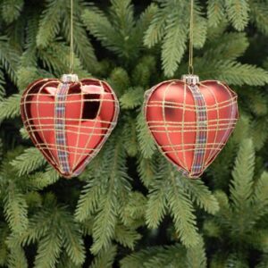 A pair heart shaped blown glass Christmas tree baubles. The one on the left is metallic red with red and blue tartan ribbon deatil around the outside edge and up the front and back finished with gold glitter check lines on top depicting tartan, the bauble on the right is the same except that it is matt red in colour.