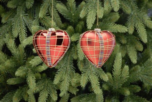 A pair heart shaped blown glass Christmas tree baubles. The one on the left is metallic red with red and blue tartan ribbon deatil around the outside edge and up the front and back finished with gold glitter check lines on top depicting tartan, the bauble on the right is the same except that it is matt red in colour.