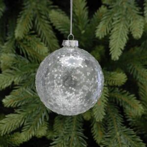 A clear glass Christmas tree bauble covered with silver glitter hanging from a tree.