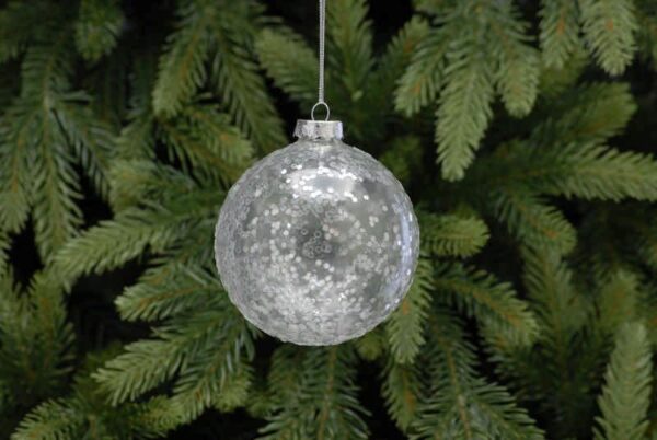 A clear glass Christmas tree bauble covered with silver glitter hanging from a tree.