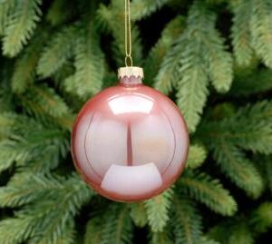 An iridescent, dusky pink, round shaped, glass Christmass tree bauble hanging from a gold string.