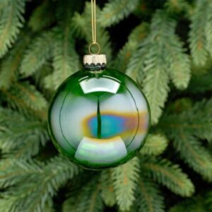 A translucent green iridescent, round shaped Christmas tree bauble hanging from a fir tree.