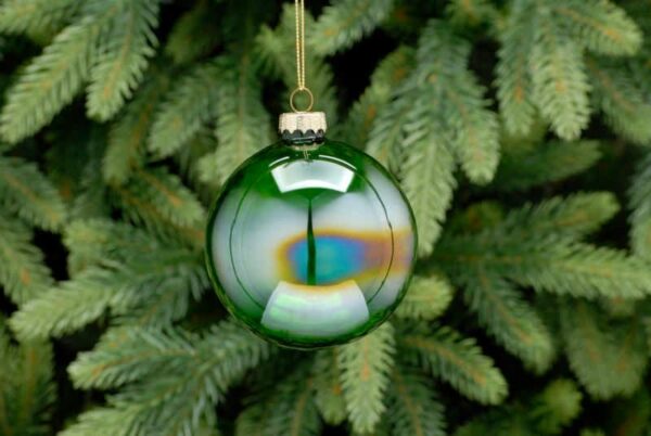 A translucent green iridescent, round shaped Christmas tree bauble hanging from a fir tree.