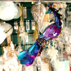 Arcylic purple iridescent peacock Christmas tree hanging decoartion. A stylized peacock with faceted wings and tail that reflect the light and enhance it's purple , petrol colours. Hanging from a silver string.