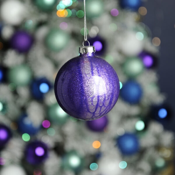 A clear glass Christmas tree bauble decorated on the inside with purple alcohol ink and filled with silver glitter creating a beautiful marble effect. hanging from a silver string.