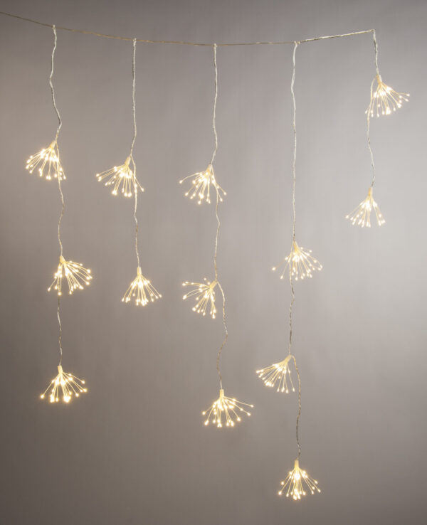 A lit set of Warm White Starburst Light Curtain lights hanging in front of a grey wall.