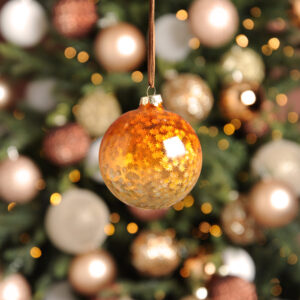 A copper and gold ombre coloured glass Christmas tree bauble filled with white star shaped sequins hanging from a brown suede string.