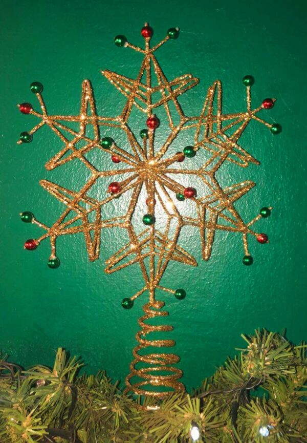 A wire frame Christmas tree topper in the shape of a six ointed snowflake. the wire frame is covered completly in gold glitter and has red and green bead on its tips and sround the centre. The snowflake sits on a conical spring for mounting on the tree.