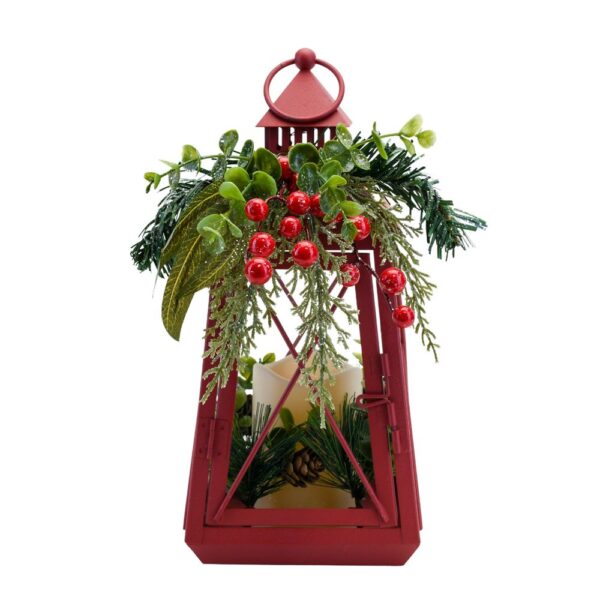 A red metal lantern with a faux candle in the centre surrounded by pinecone and fir sprigs. The top of the lantern is decorated with green foliage and red berries.