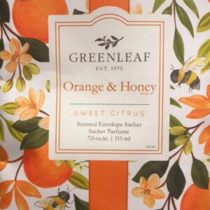 An Orange & Honey fragranced scent sachet showing a painted image of an orange tree with ripe oranges, orange blossom, green leaves and honey bees. An orange band runs vertivally down the middle of the image and on top of the band sits a cream coloured box. At the top of the box in black is the logo for the Greenleaf Company and beneath that in orange is text that reads 'Orange & Honey™ SWEET CITRUS' and in black beneath that 'Scented Envelope Sachet Sachet Parfume 7.0CU.IM. 115ML'.