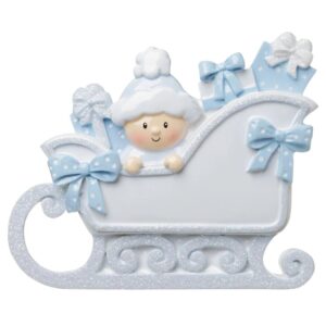 Baby In A Sleigh (Blue) Personalised Christmas Decoration. A white sleigh decorated with ale blue ididescent glitter and blue polka dot bows. Inside the sleigh there is a baby wearing a pale blue Santa hat sitting amonst some pale blue presents.