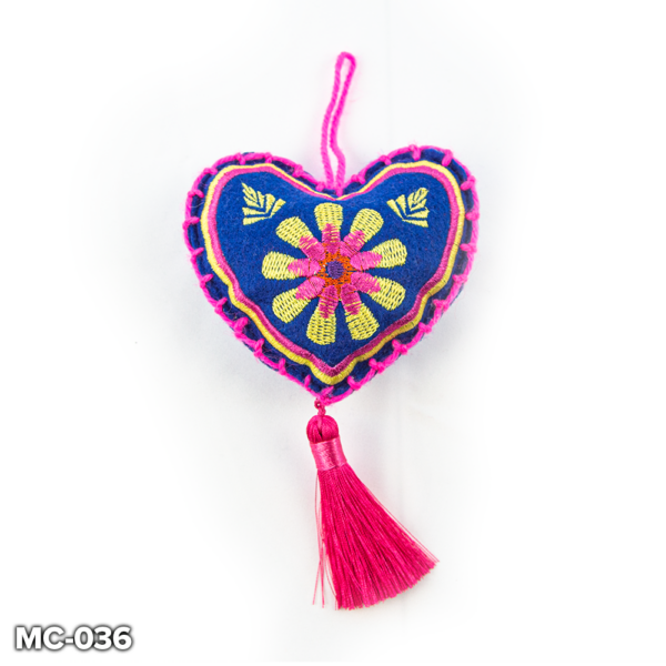 A blue felt, heart shaped Christmas tree decoration. This blue felt heart has a yellow and pink flower embroidered in the centre and yellow and pink stitching around the outside. At the top there is a loop of pink wool for hanging and a pink tassel hangs from the point of the heart.