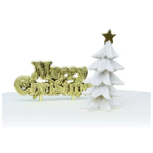 A white, polyresin Christmas tree topped with a gold star cake decoration next to a gold Merry Christmas sign cake decoration.