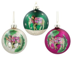 A set of three glass Christmas baubles featuring Exotic elephants. The bauble on the left is pale gold coloured and has an antique glass finish. It has an image of an exotic elephant, decorated with pink flowers with butterfly wings for ears surrounded by two large palm leaves. The bauble in the centre is dark green coloured and has an antique glass finish. It has an image of an exotic elephant, decorated with pink flowers with butterfly wings for ears walking on an gold glitter base with gold glitter stars around it. The bauble on the right is magenta pink coloured and has an antique glass finish. It has an image of an exotic elephant, decorated with pink flowers with butterfly wings for ears surrounded by two large palm leaves. All are hanging from gold strings.