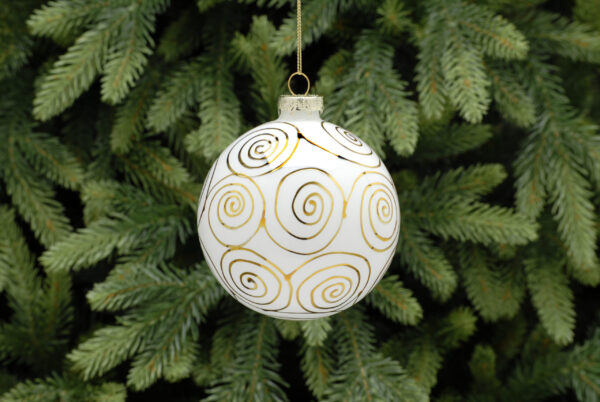 A white glass Christmas tree bauble decorated with metallic gold swirls all over. hanging from a gold string.