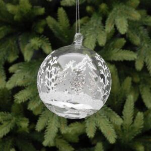 A clear glass Christmas tree bauble decorated with a winter forest scene in white and silver glitter. Hanging from a silver thread.