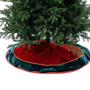 A large red velour Christmas tree skirt with a dark green border and gold cord detail finished with a festive red trim beneath a green Christmas tree.