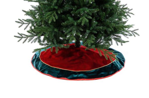 A large red velour Christmas tree skirt with a dark green border and gold cord detail finished with a festive red trim beneath a green Christmas tree.