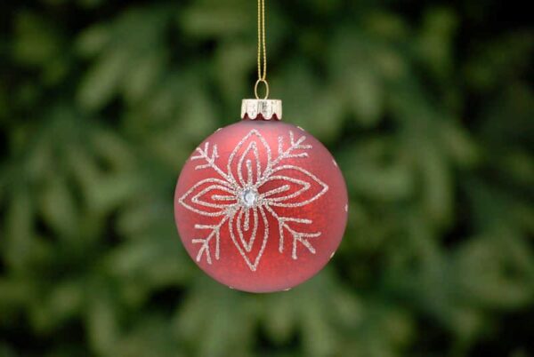 An antique red, glass Christmas tree bauble decorated with fine silver glitter lines in a floral snowflake pattern with a white diamante jewel in the centre.