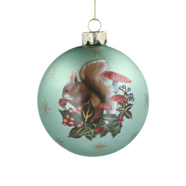 A matt pale green, glass Christmas tree bauble decorated with ahand painted image of a red squirrel nestled amongst a group of red and white toadstools and festive foliage. It is surrounded by gold stars.