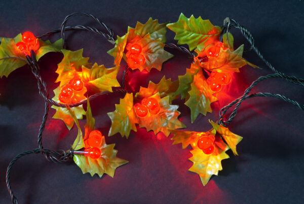 An illuminated string of 100 LED Red Berry lights with green fabric holly leaves.