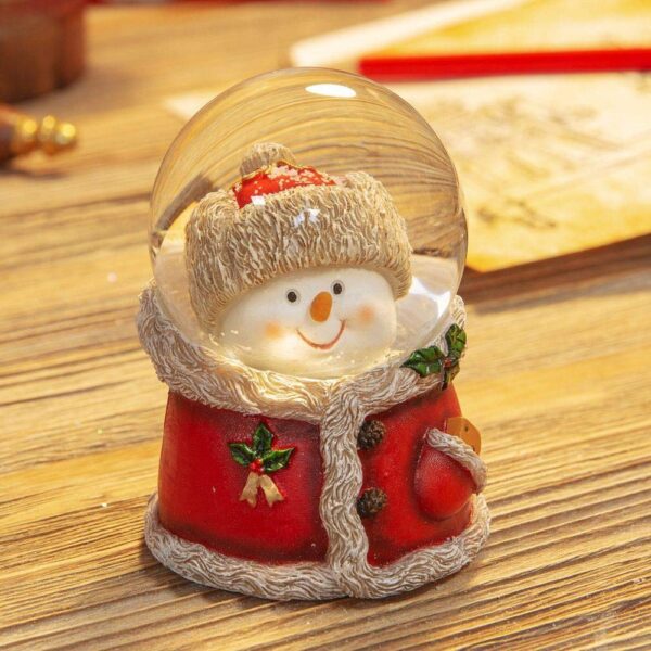 A snowman snowglobe. The polyresin base of this snow globe is in the shape of a red fur lined jacket with holly decorations. Inside the glass globe is the head of the snowman, he has a carrot for a nose and is wearing a red fur trimmed hat that matches the jacket.