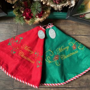 A pair of 80cm Embroidered Felt Tree Skirts in Red or Green. Both with a decorative Merry Christmas message, in gold, with a decorative swirl, holly and starburst. Trimmed with red and white candy cane style fabric. background, with a decorative Merry Christmas message, in gold, with a decorative swirl, holly and starburst. Hemmed with red and white candy cane style ribbon.