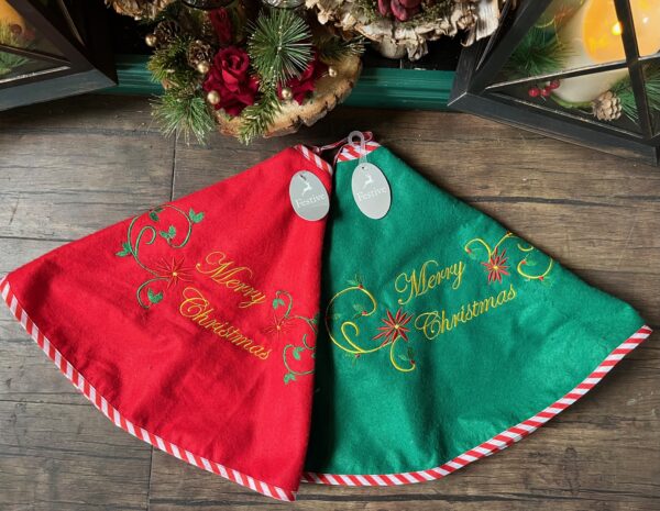 A pair of 80cm Embroidered Felt Tree Skirts in Red or Green. Both with a decorative Merry Christmas message, in gold, with a decorative swirl, holly and starburst. Trimmed with red and white candy cane style fabric. background, with a decorative Merry Christmas message, in gold, with a decorative swirl, holly and starburst. Hemmed with red and white candy cane style ribbon.