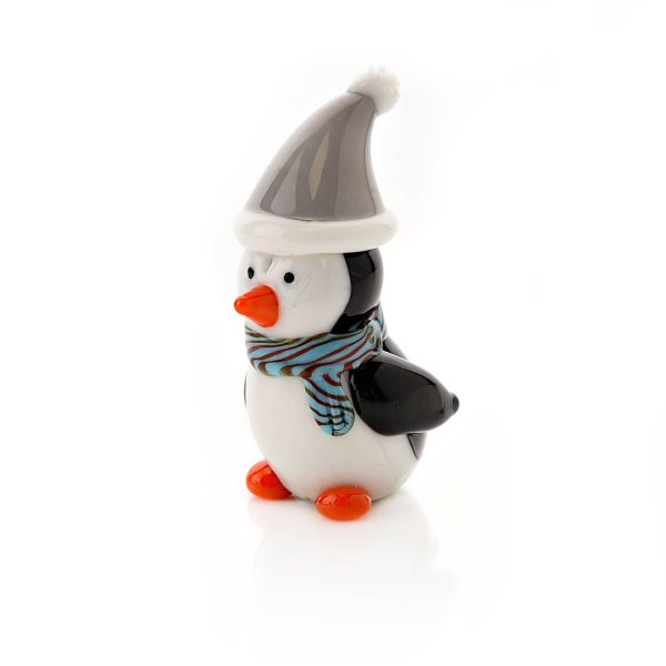 Image shows a 4 cm tall hand blown glass penguin figurine. His body and head are made from white glass, his wings and eyes are black and his beak and feet are bright orange. He wears a grey and white stripy scarf and matching Santa hat. Shown against a white background.