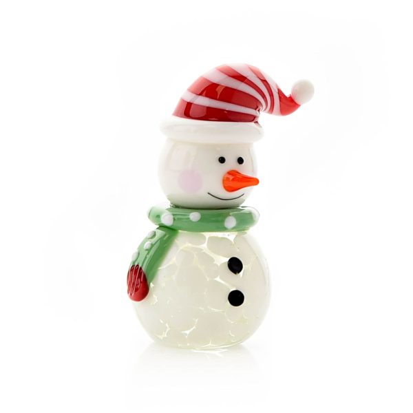 A hand finished blown glass ornament of a snowman. He has a round body of white glass white two dots of black for buttons. His round head has two black dots of 'coal' for eyes and a bright orange carrot nose and a lovely wide smile. He is wearing an adorable red and white stripey santa hat and green polka dot scarf. Shown on a white background.