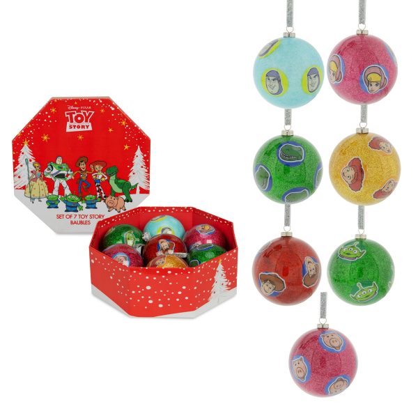 On the left of the image there is an octagonal red gift box decorated in a festive scene. Inside the box sits 7 colourful Christmas baubles. Behind the box, the lid shows the characters from Disney's Toy Story. On the right side we can see a close up of all the baubles in the box. The Characters faces are repeated around each bauble with each character having a different coloured glittery background. Buzz Lightyear is on a pale turquoise, Woody on red, Beau Peep is on Pink, Jessie is on Yellow, Rex is on green, Ham on Pink and Alien on green, Each bauble hangs from a silver glitter ribbon.