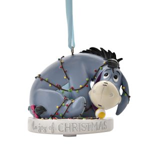 A polyresin Christmas tree decoration depicting Eyeore from Disney's Winnie the Pooh tangled up in a string of festive lights. He sits upon a white plinth that has silver text around it that reads 'The joy of Christmas' and hangs from a silver ribbon.